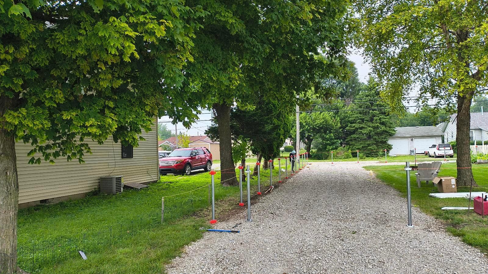 Galvanized steel fence posts and mounted brackets along a gravel driveway in Kokomo, before vinyl sleeves are installed.