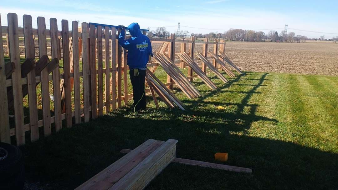 Ideal Fence installer fastening vertical wood pickets to a post-and-rail fence frame supported by temporary braces.